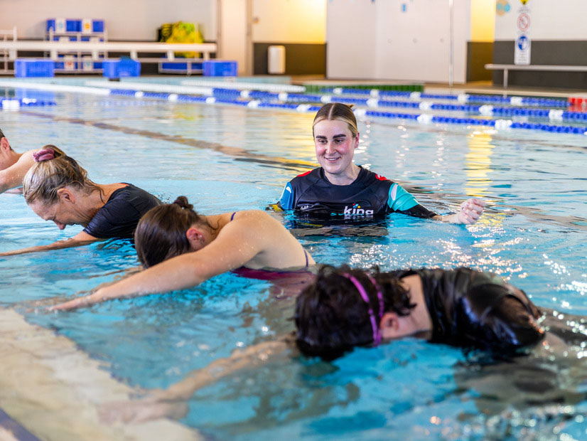 A Kingswim instructor is helping an adult with their swimming stroke technique