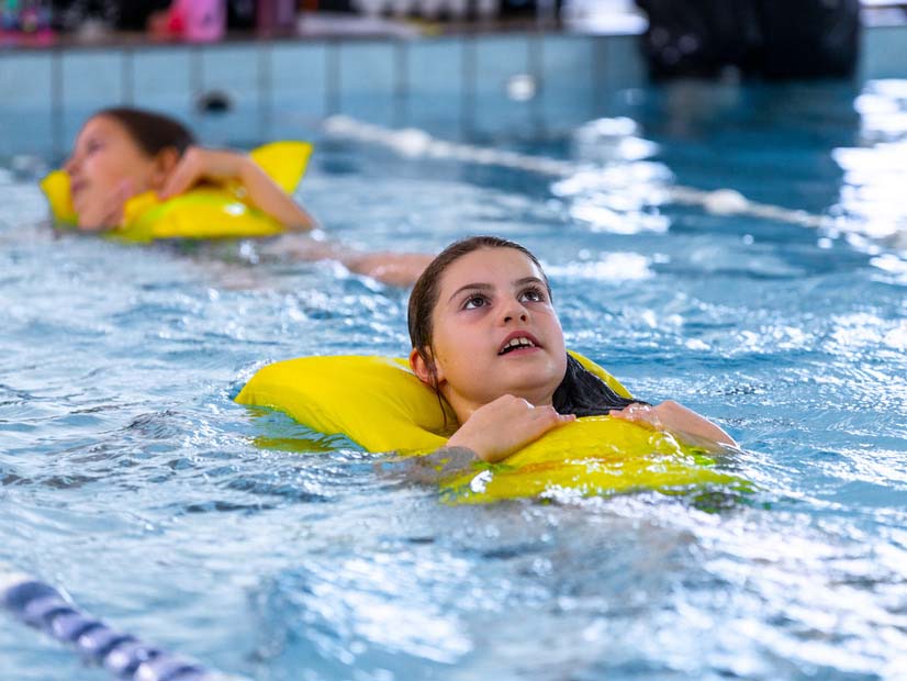 Girl floating in swimming pool wearing a life jacket