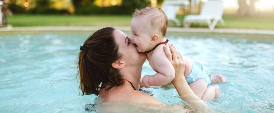 A woman in the swimming pool with her baby in her arms.