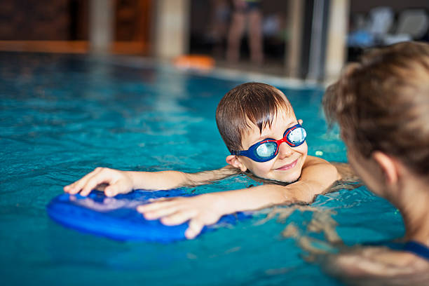 A boy wearing goggles learning to swim with his swimming teacher